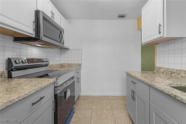 kitchen with light tile patterned floors, light stone counters, visible vents, baseboards, and appliances with stainless steel finishes