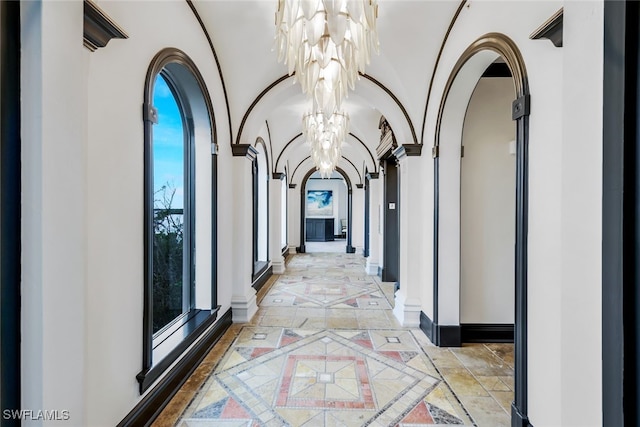 hall featuring stone tile floors, baseboards, an inviting chandelier, lofted ceiling, and arched walkways