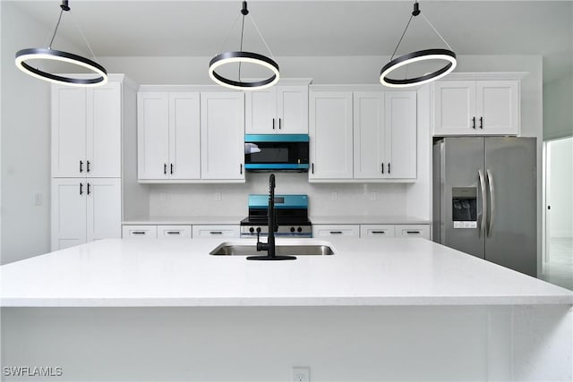 kitchen with a kitchen island with sink, stainless steel appliances, a sink, white cabinets, and hanging light fixtures