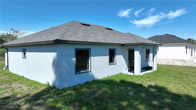 back of property featuring stucco siding, a shingled roof, and a yard