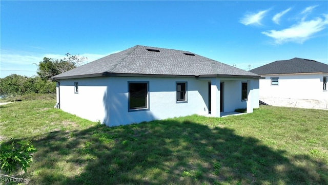 back of house with roof with shingles, a lawn, and stucco siding