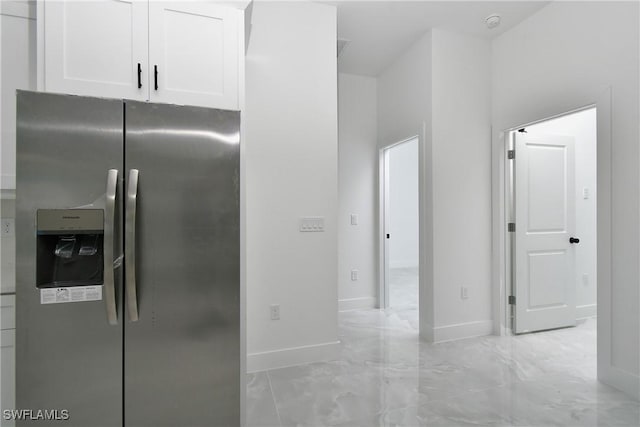 kitchen with marble finish floor, stainless steel fridge, baseboards, and white cabinets