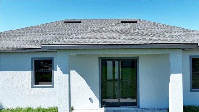 rear view of house featuring a shingled roof and stucco siding