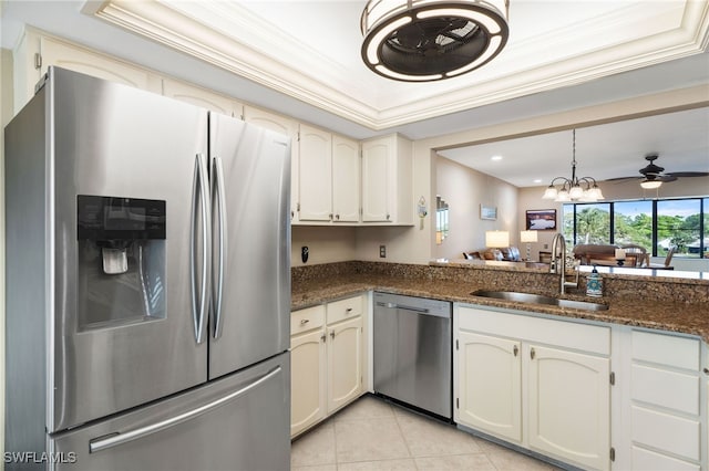 kitchen with sink, a raised ceiling, dark stone countertops, ceiling fan with notable chandelier, and appliances with stainless steel finishes