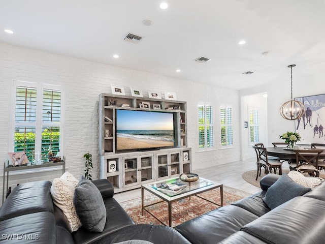 living room with light hardwood / wood-style flooring, a notable chandelier, a wealth of natural light, and brick wall