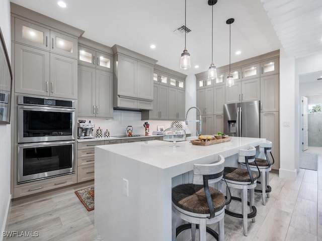 kitchen featuring pendant lighting, a kitchen island with sink, gray cabinetry, stainless steel appliances, and a kitchen bar