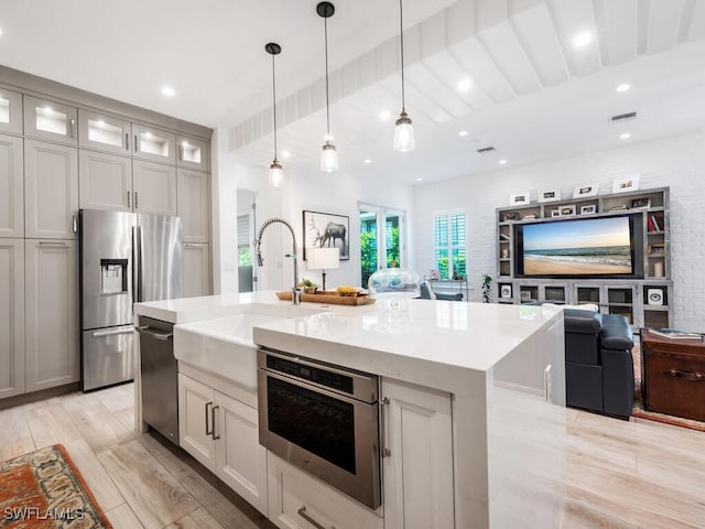 kitchen with sink, hanging light fixtures, light wood-type flooring, stainless steel appliances, and a kitchen island with sink