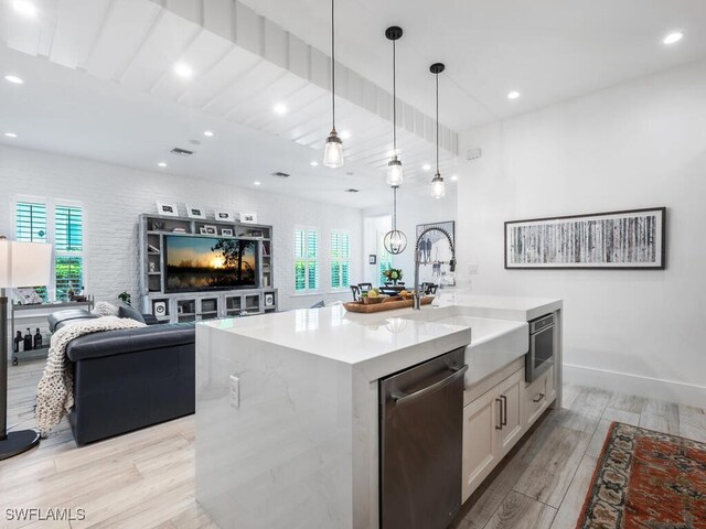 kitchen featuring white cabinetry, decorative light fixtures, a center island with sink, light hardwood / wood-style flooring, and stainless steel dishwasher