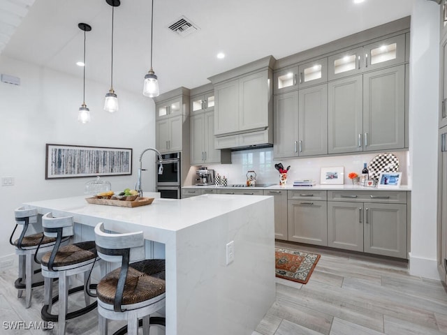 kitchen featuring gray cabinets, a breakfast bar, hanging light fixtures, a center island with sink, and decorative backsplash