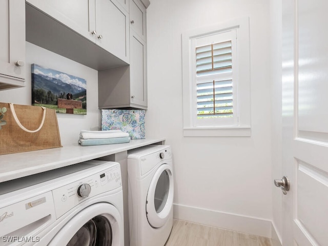 clothes washing area with cabinets, washing machine and clothes dryer, and light wood-type flooring