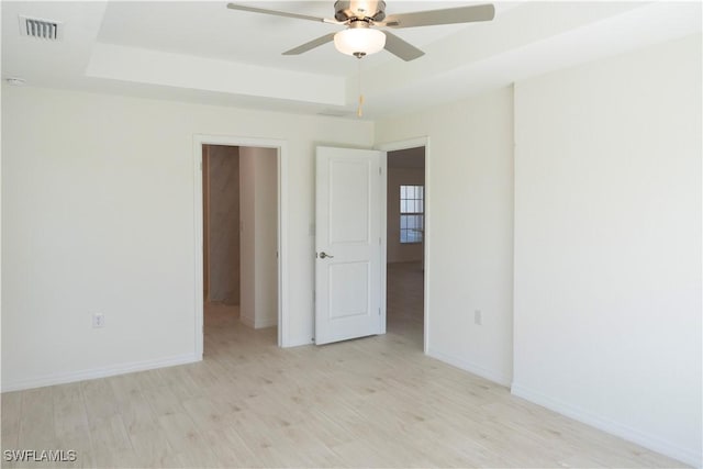 spare room with a tray ceiling, ceiling fan, and light hardwood / wood-style floors