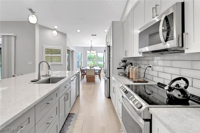 kitchen with light stone countertops, sink, stainless steel appliances, tasteful backsplash, and pendant lighting