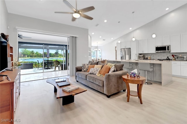 living room featuring ceiling fan with notable chandelier, light hardwood / wood-style floors, sink, and high vaulted ceiling