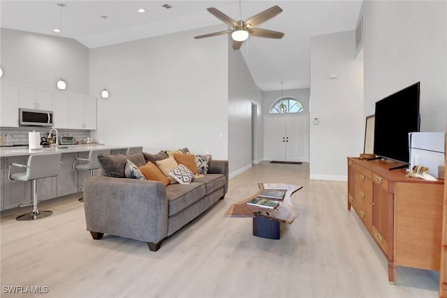 living room featuring ceiling fan, sink, high vaulted ceiling, and light wood-type flooring