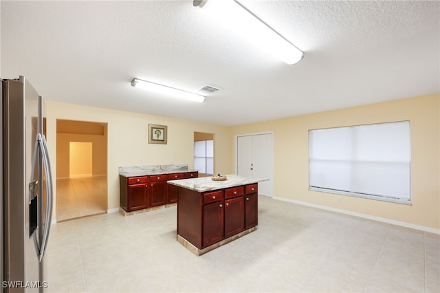 kitchen featuring a center island, stainless steel fridge, light stone counters, and a textured ceiling