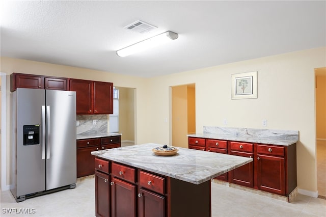 kitchen with decorative backsplash, a kitchen island, light stone counters, and stainless steel fridge with ice dispenser