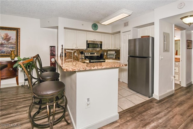 kitchen with kitchen peninsula, appliances with stainless steel finishes, light stone counters, a textured ceiling, and sink