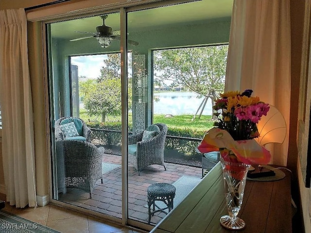 doorway with a water view, light tile patterned floors, and ceiling fan