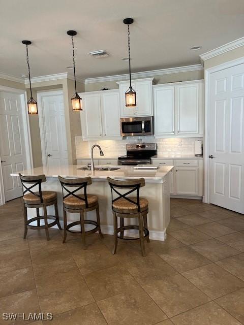 kitchen with a kitchen bar, sink, white cabinets, stainless steel appliances, and a center island with sink