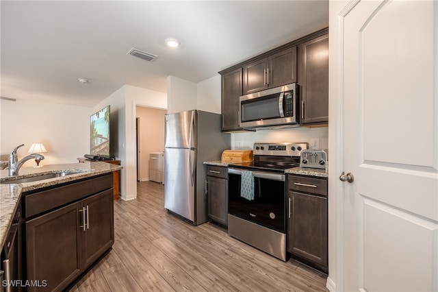 kitchen with dark brown cabinets, light wood-type flooring, stainless steel appliances, and sink