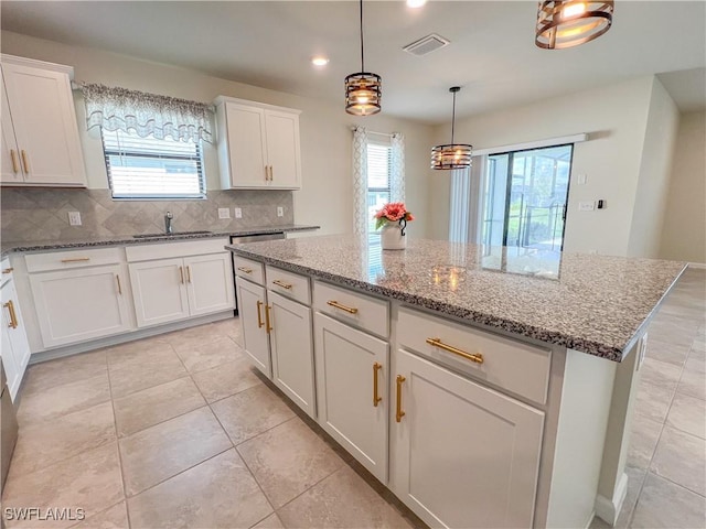 kitchen with decorative backsplash, light tile patterned floors, white cabinets, a kitchen island, and hanging light fixtures