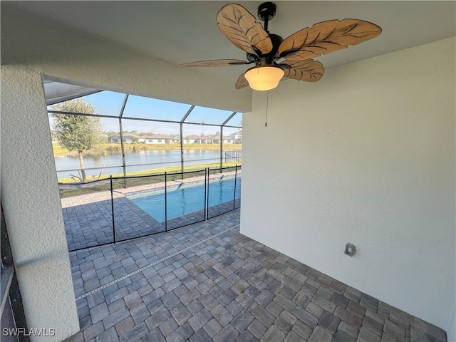 view of swimming pool with a patio area, ceiling fan, a water view, and glass enclosure