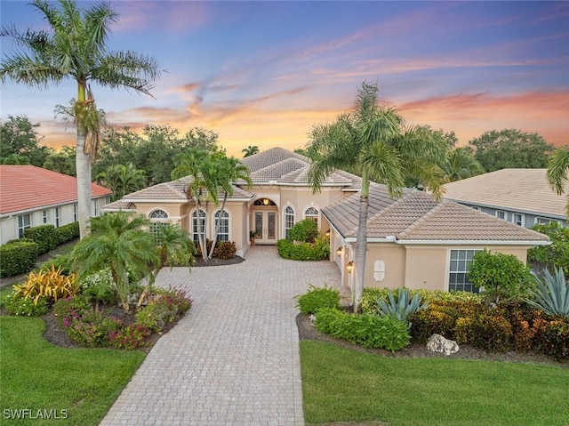 mediterranean / spanish-style home featuring a front lawn, a tiled roof, stucco siding, french doors, and decorative driveway