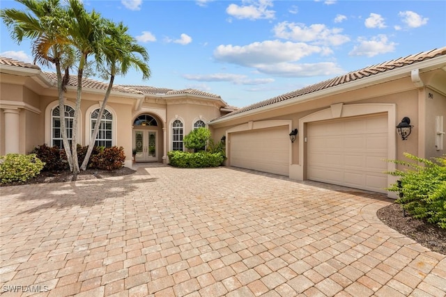 mediterranean / spanish house with an attached garage, stucco siding, french doors, a tiled roof, and decorative driveway