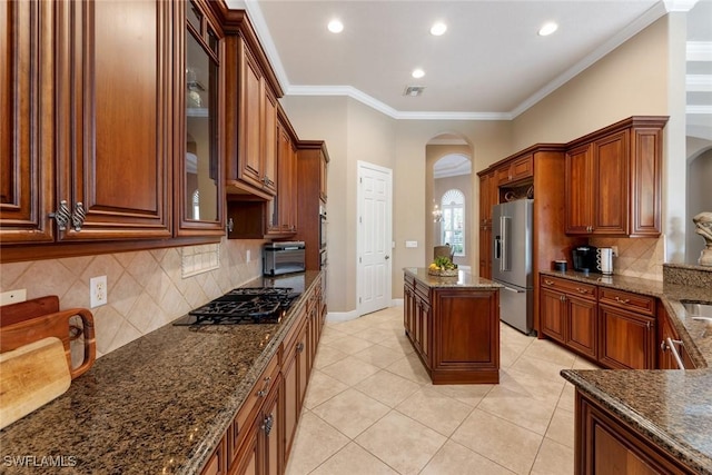 kitchen featuring light tile patterned floors, high quality fridge, gas stovetop, dark stone countertops, and ornamental molding