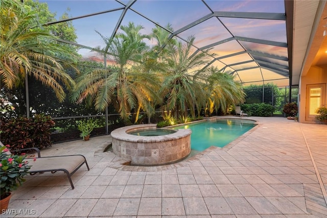 pool at dusk featuring glass enclosure, an in ground hot tub, and a patio