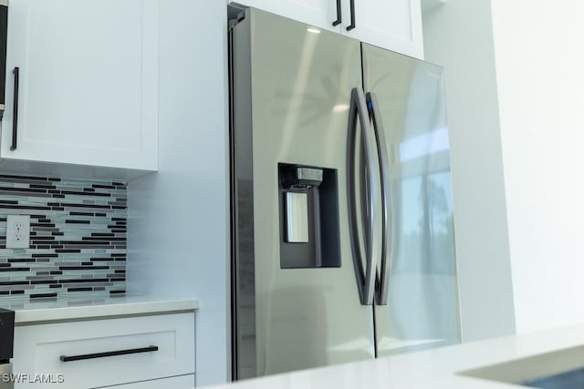 interior details featuring backsplash, stainless steel fridge, and white cabinets