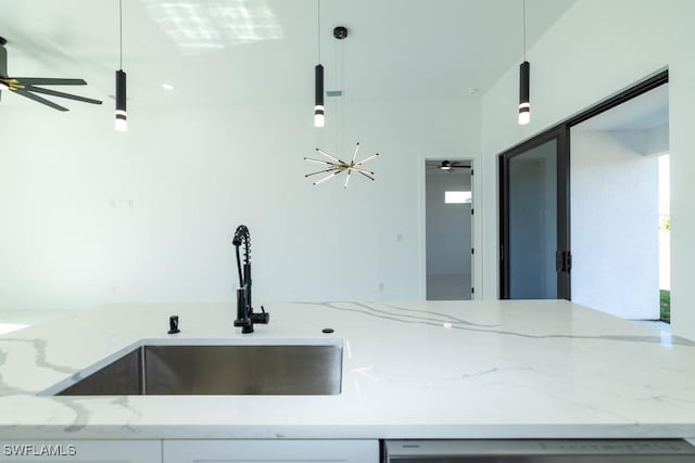 kitchen with light stone countertops, sink, white cabinets, and decorative light fixtures