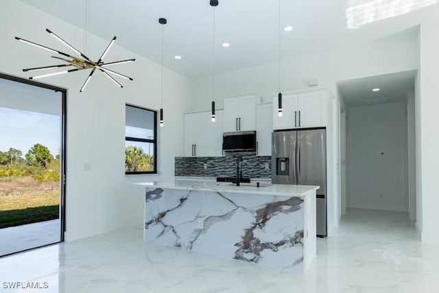 kitchen with white cabinetry, stainless steel appliances, decorative light fixtures, and an island with sink