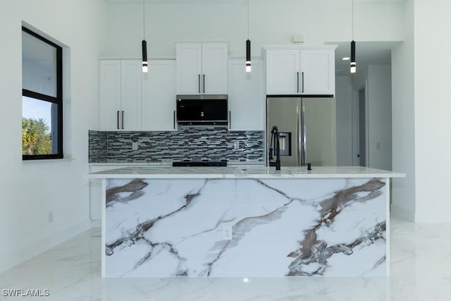 kitchen with a center island with sink, hanging light fixtures, stainless steel fridge, light stone countertops, and white cabinets