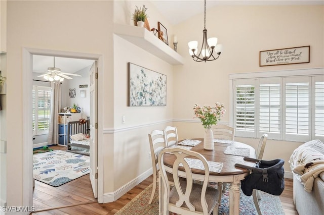 dining area featuring high vaulted ceiling, wood-type flooring, and ceiling fan with notable chandelier