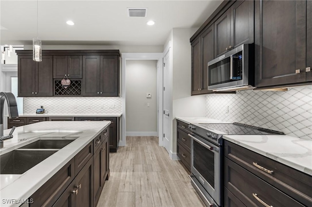 kitchen featuring sink, stainless steel appliances, light hardwood / wood-style flooring, decorative light fixtures, and dark brown cabinets