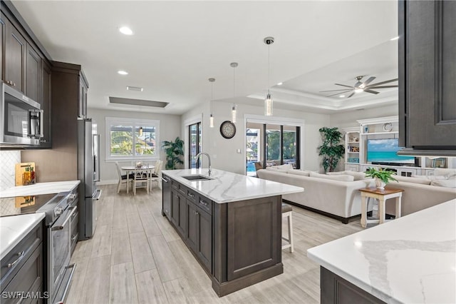 kitchen featuring stainless steel appliances, ceiling fan, a kitchen island with sink, sink, and hanging light fixtures