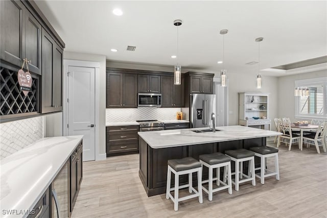 kitchen with decorative light fixtures, stainless steel appliances, a breakfast bar area, and an island with sink