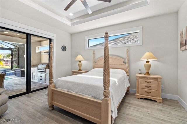 bedroom with hardwood / wood-style floors, access to outside, ceiling fan, and a tray ceiling