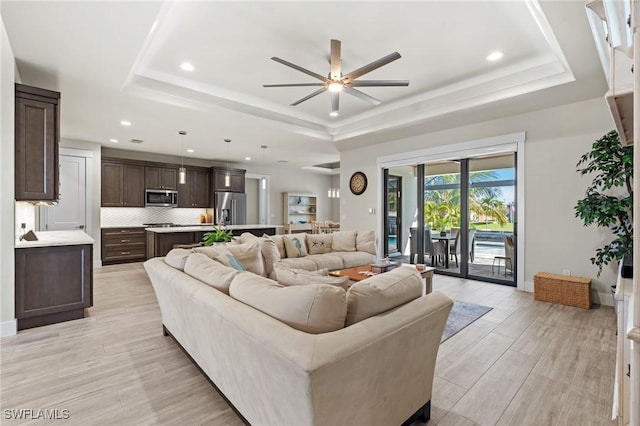 living room with a tray ceiling, ceiling fan, and light hardwood / wood-style flooring