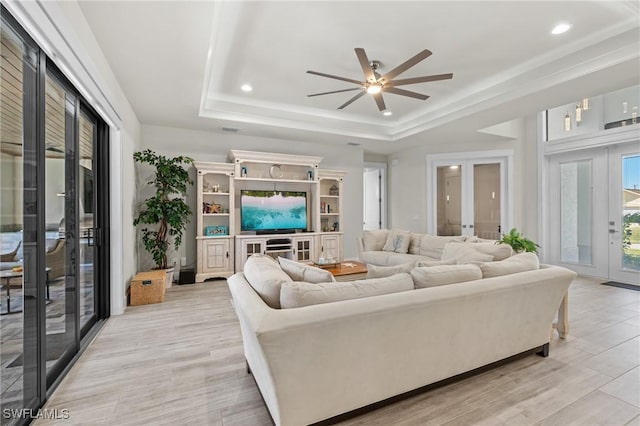 living room with ceiling fan, light hardwood / wood-style flooring, a tray ceiling, and french doors