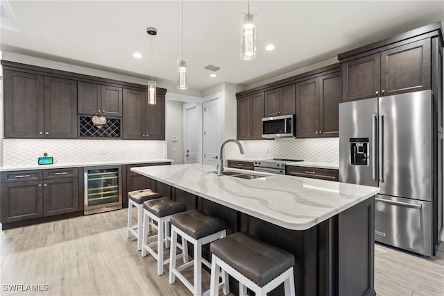 kitchen with hanging light fixtures, sink, an island with sink, stainless steel appliances, and beverage cooler