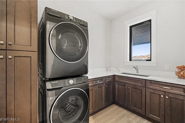 laundry area featuring cabinets, stacked washing maching and dryer, sink, and light wood-type flooring