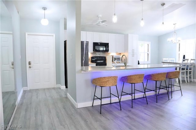 kitchen with white cabinetry, light hardwood / wood-style floors, a breakfast bar area, black appliances, and ceiling fan with notable chandelier