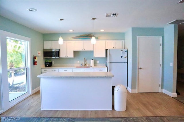 kitchen with light wood-type flooring, sink, decorative light fixtures, white cabinets, and white fridge