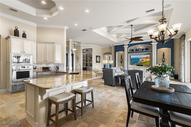 kitchen featuring appliances with stainless steel finishes, a breakfast bar, ornamental molding, coffered ceiling, and light stone counters