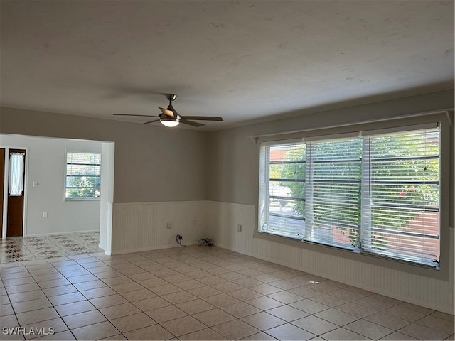 empty room featuring ceiling fan, plenty of natural light, light tile patterned flooring, and wainscoting