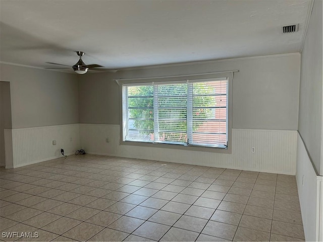 unfurnished room with light tile patterned flooring, a wainscoted wall, ceiling fan, and visible vents