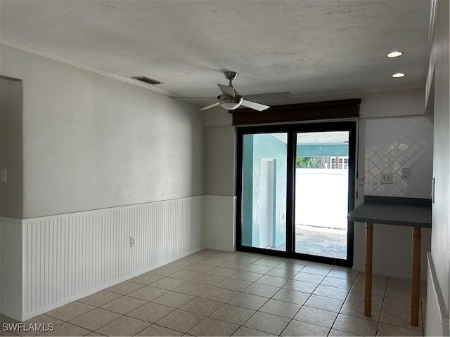 spare room featuring visible vents, crown molding, a wainscoted wall, light tile patterned flooring, and a ceiling fan