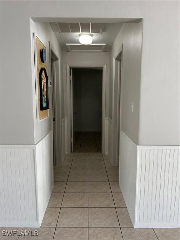 hall featuring light tile patterned flooring and wainscoting